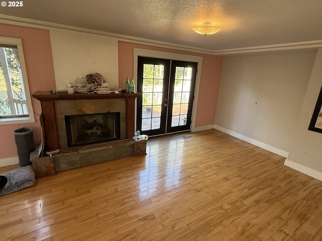 unfurnished living room with french doors, a tiled fireplace, a textured ceiling, and light wood-type flooring