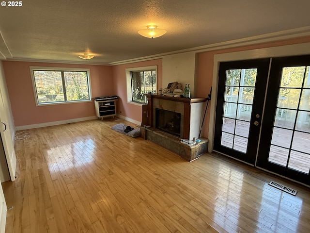 unfurnished living room featuring french doors, a fireplace, light hardwood / wood-style flooring, and a textured ceiling