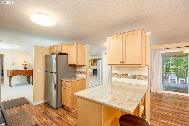 kitchen with light brown cabinetry, decorative backsplash, freestanding refrigerator, and wood finished floors