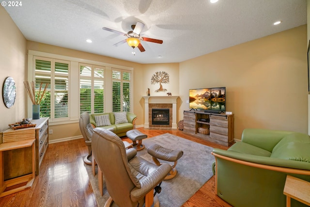 living room featuring a tile fireplace, a textured ceiling, ceiling fan, and light wood-type flooring