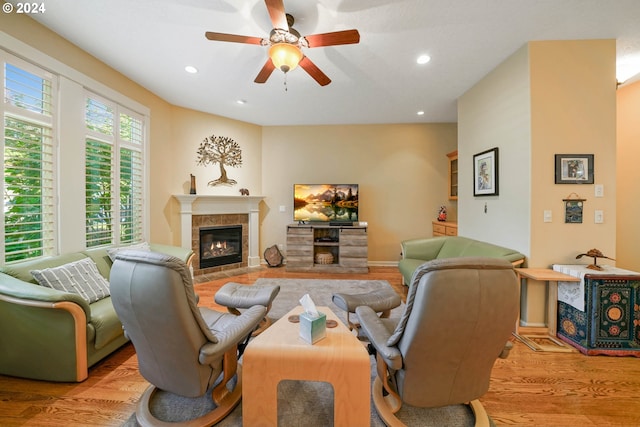 living room featuring a tile fireplace, ceiling fan, and light wood-type flooring