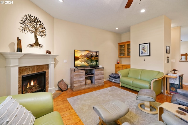 living room with a tiled fireplace, ceiling fan, and light wood-type flooring