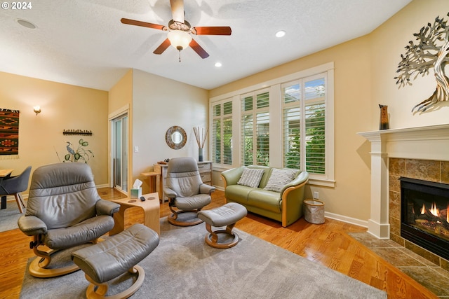 living room with a tile fireplace, ceiling fan, a textured ceiling, and light hardwood / wood-style floors