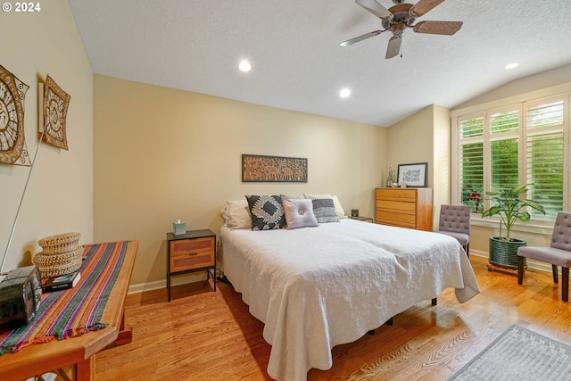 bedroom with ceiling fan, vaulted ceiling, light hardwood / wood-style floors, and a textured ceiling