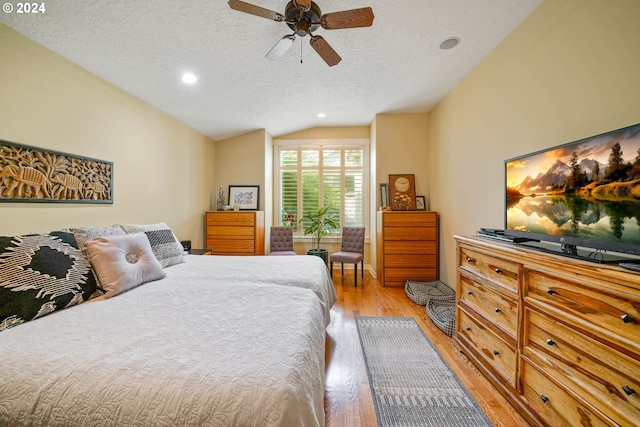 bedroom featuring ceiling fan, lofted ceiling, a textured ceiling, and light hardwood / wood-style floors