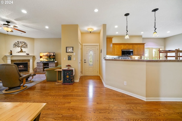 kitchen with pendant lighting, a tiled fireplace, wood-type flooring, and ceiling fan