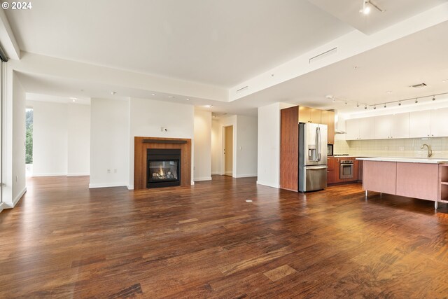 unfurnished living room with rail lighting and dark wood-type flooring