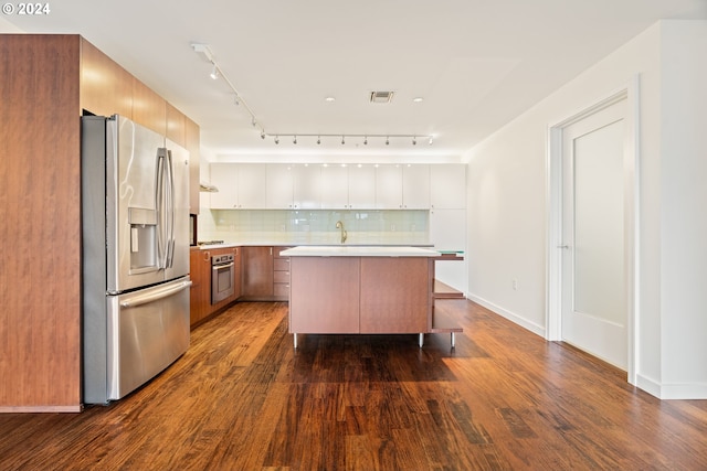 kitchen with an island with sink, stainless steel appliances, track lighting, decorative backsplash, and wood-type flooring