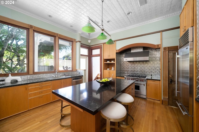 kitchen with high end appliances, crown molding, sink, a kitchen island, and hanging light fixtures