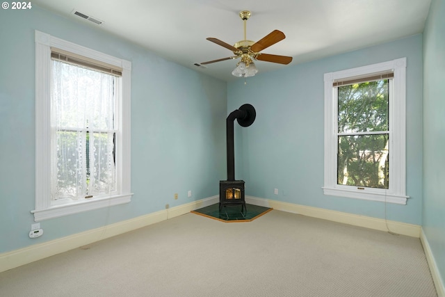 unfurnished living room with carpet flooring, ceiling fan, plenty of natural light, and a wood stove