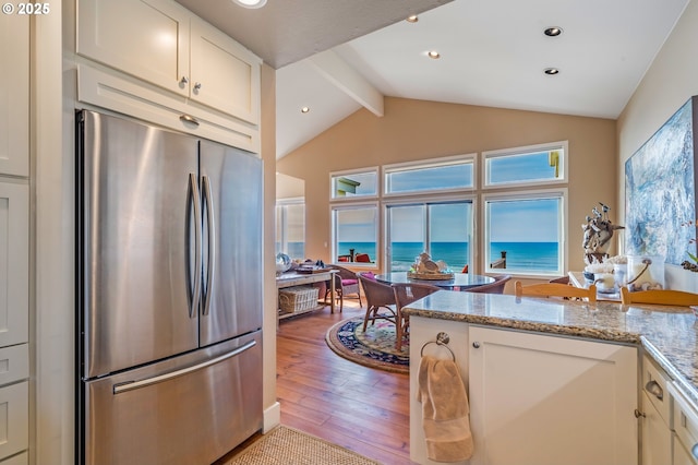 kitchen featuring stainless steel refrigerator, vaulted ceiling with beams, white cabinets, light stone counters, and a water view