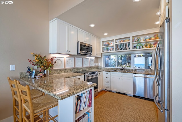 kitchen with stone countertops, kitchen peninsula, white cabinets, and appliances with stainless steel finishes