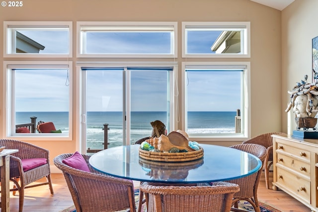 dining area with a water view, vaulted ceiling, and light wood-type flooring