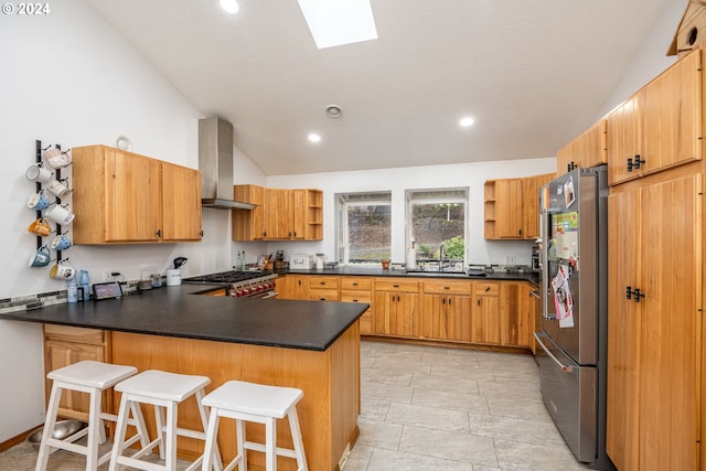 kitchen featuring kitchen peninsula, wall chimney exhaust hood, vaulted ceiling with skylight, a breakfast bar, and stainless steel appliances