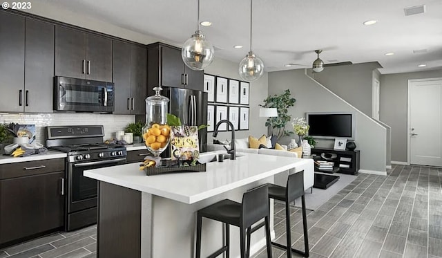 kitchen with a kitchen island with sink, a kitchen breakfast bar, sink, decorative backsplash, and appliances with stainless steel finishes