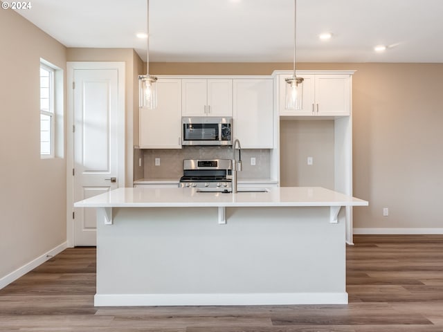 kitchen with tasteful backsplash, stainless steel appliances, a kitchen island with sink, decorative light fixtures, and light hardwood / wood-style floors