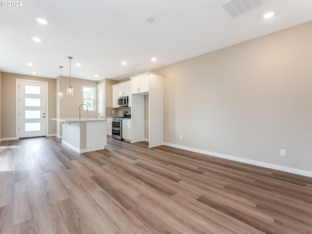 kitchen featuring white cabinetry, hanging light fixtures, a kitchen island with sink, appliances with stainless steel finishes, and light wood-type flooring