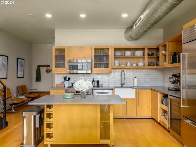 kitchen with open shelves, appliances with stainless steel finishes, glass insert cabinets, a kitchen island, and a sink