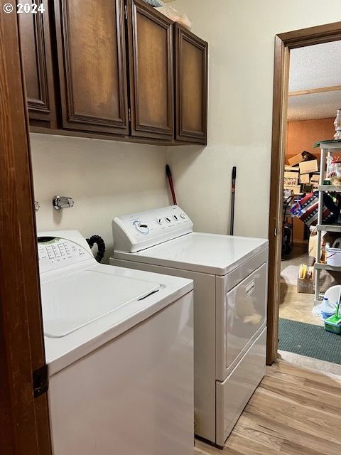 clothes washing area with washer and dryer, light hardwood / wood-style floors, and cabinets