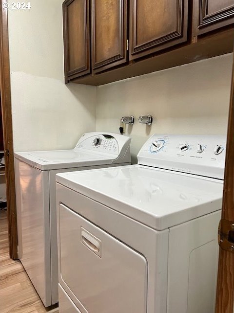 laundry room featuring washing machine and clothes dryer, cabinets, and light hardwood / wood-style flooring