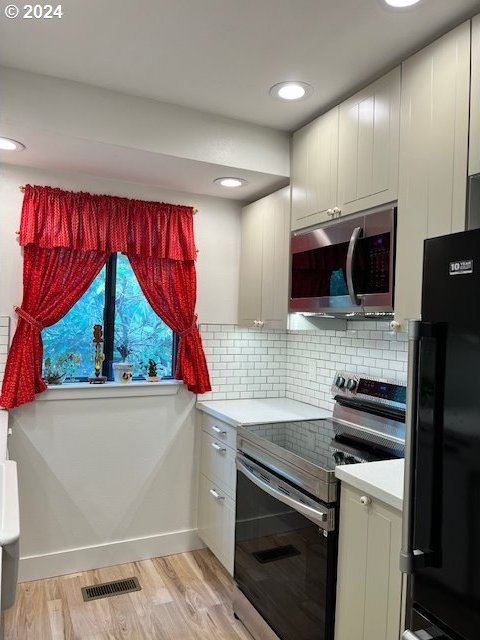 kitchen with white cabinets, appliances with stainless steel finishes, light hardwood / wood-style floors, and backsplash