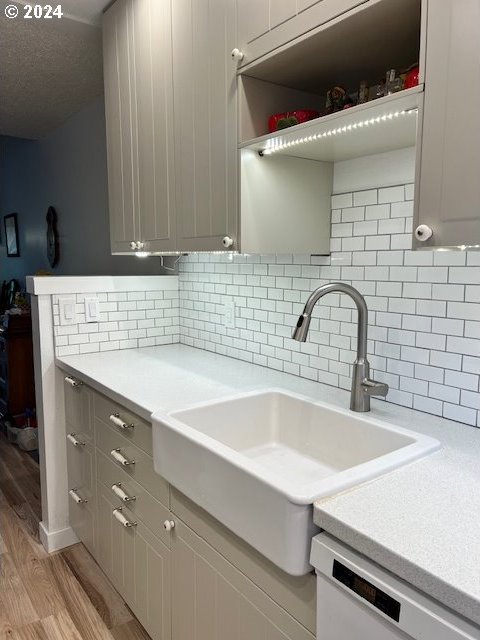 kitchen featuring dishwasher, gray cabinets, light hardwood / wood-style floors, decorative backsplash, and sink