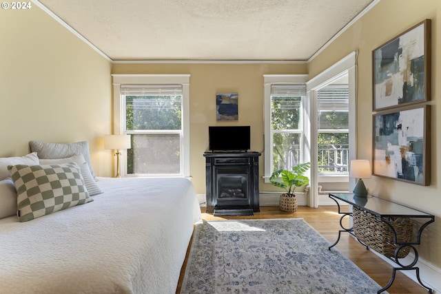 bedroom with multiple windows, wood-type flooring, ornamental molding, and a textured ceiling