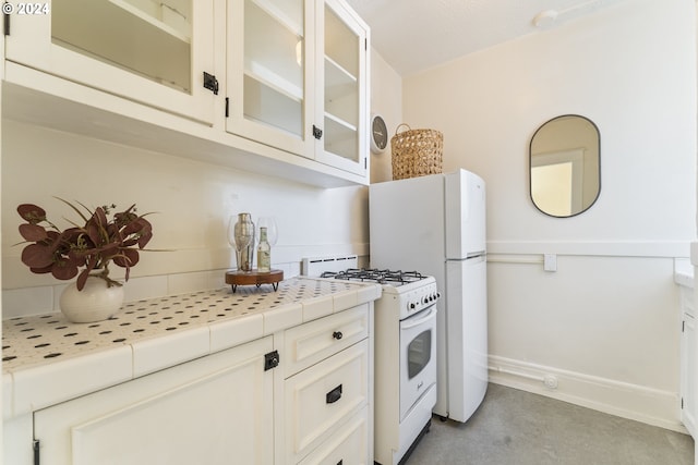 kitchen with tile counters, white gas range oven, and white cabinetry