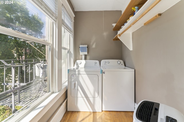 clothes washing area with a healthy amount of sunlight, washing machine and dryer, and light hardwood / wood-style floors