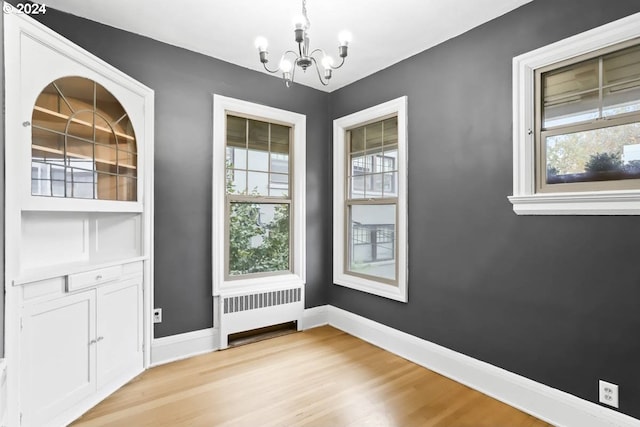 unfurnished dining area with light hardwood / wood-style flooring, a notable chandelier, and radiator