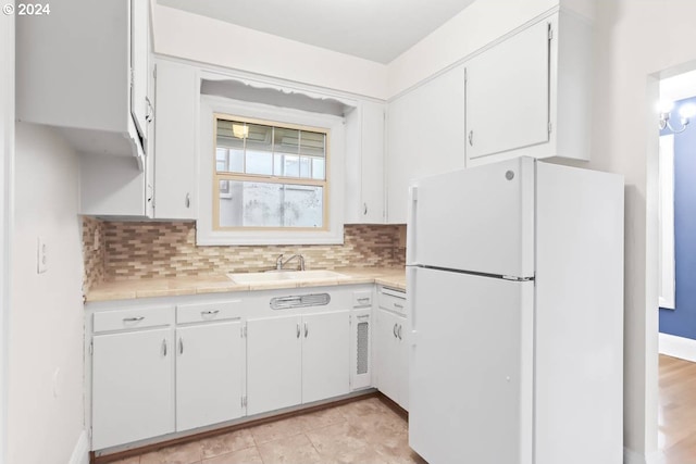 kitchen featuring white fridge, white cabinetry, backsplash, tile counters, and sink