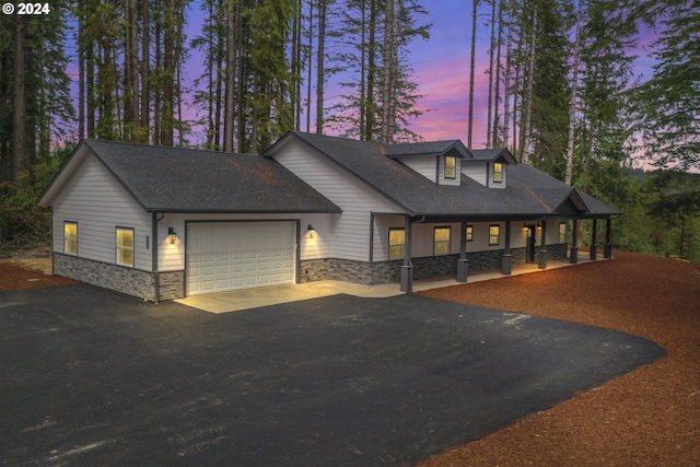 6018 Little Woahink Dr, Florence, OR 97439 - view of front of home with stone siding, driveway, an attached garage, covered porch, and a shingled roof