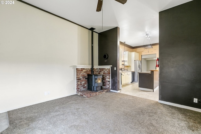 unfurnished living room with a wood stove, light carpet, crown molding, and ceiling fan