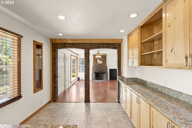 kitchen featuring a fireplace, a textured ceiling, ceiling fan, light brown cabinets, and light hardwood / wood-style floors