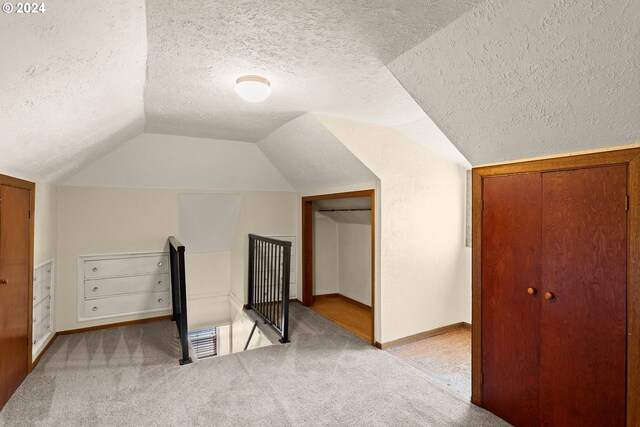 bonus room with lofted ceiling, light carpet, and a textured ceiling