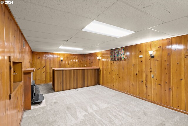 basement featuring carpet flooring, wooden walls, and a drop ceiling