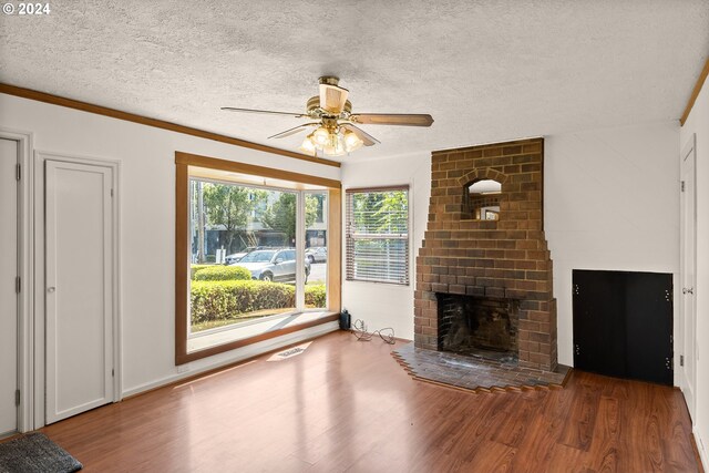 unfurnished living room featuring crown molding, a brick fireplace, hardwood / wood-style floors, ceiling fan, and a textured ceiling