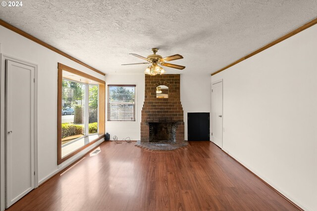 unfurnished living room with a textured ceiling, a fireplace, dark wood-type flooring, ornamental molding, and ceiling fan