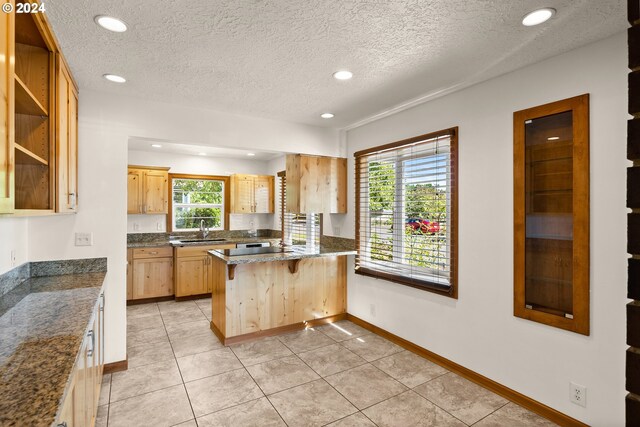 kitchen featuring light brown cabinetry, dark stone counters, kitchen peninsula, a kitchen breakfast bar, and a textured ceiling