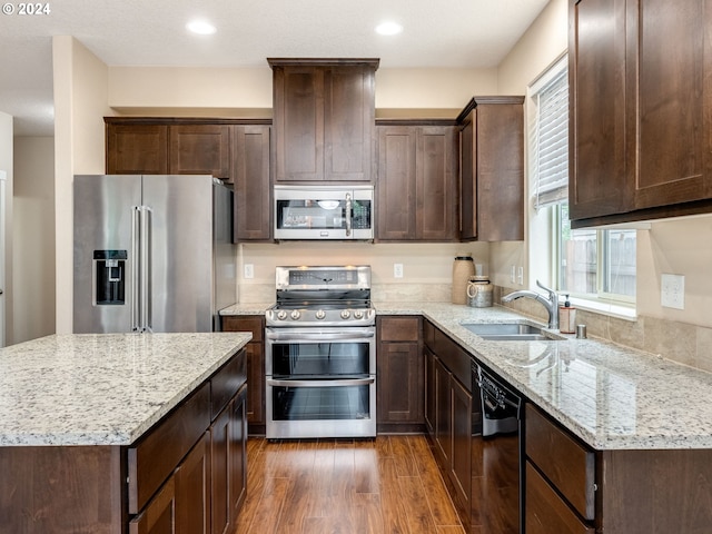 kitchen with dark wood-type flooring, sink, light stone countertops, appliances with stainless steel finishes, and a kitchen island