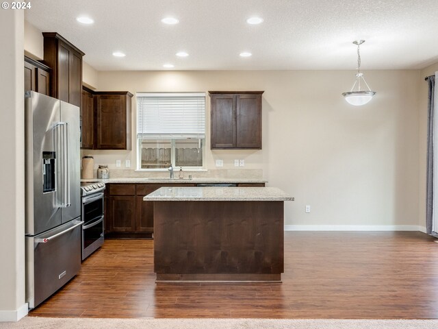 kitchen with a center island, dark wood-type flooring, light stone counters, pendant lighting, and appliances with stainless steel finishes