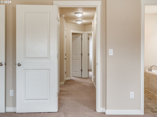 hallway with light colored carpet and a textured ceiling