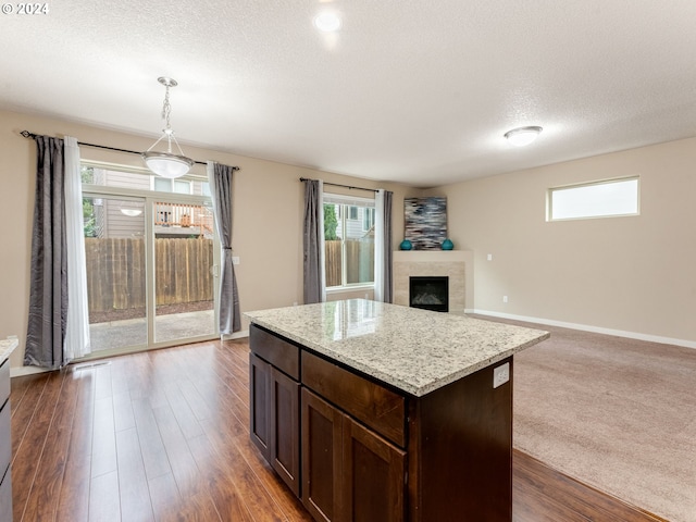 kitchen with dark wood-type flooring, light stone counters, pendant lighting, a textured ceiling, and a tiled fireplace