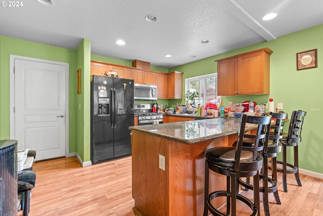 kitchen with kitchen peninsula, a textured ceiling, light hardwood / wood-style flooring, appliances with stainless steel finishes, and dark stone countertops