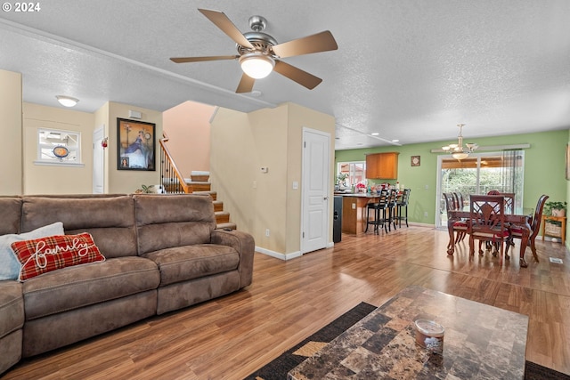 living room with ceiling fan with notable chandelier, light hardwood / wood-style flooring, and a textured ceiling