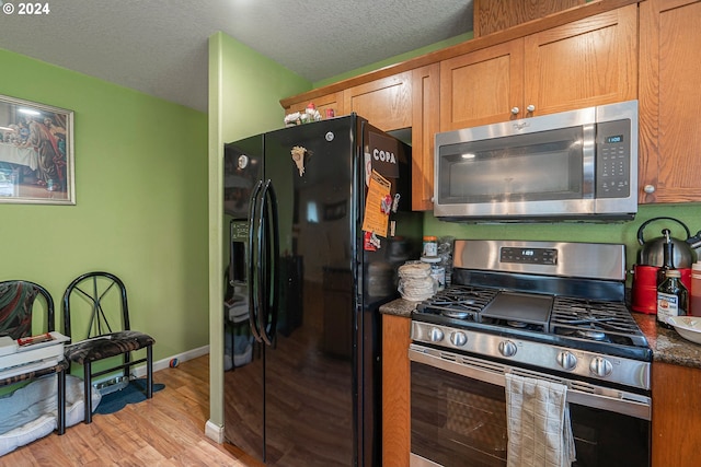 kitchen featuring appliances with stainless steel finishes, dark stone countertops, a textured ceiling, and light hardwood / wood-style flooring