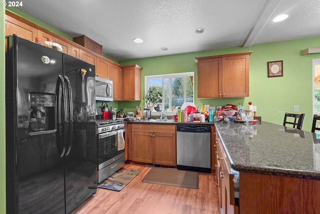 kitchen featuring kitchen peninsula, a textured ceiling, appliances with stainless steel finishes, dark stone countertops, and light hardwood / wood-style floors