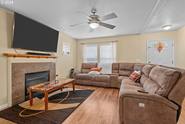 living room featuring ceiling fan, a tiled fireplace, hardwood / wood-style flooring, and a textured ceiling