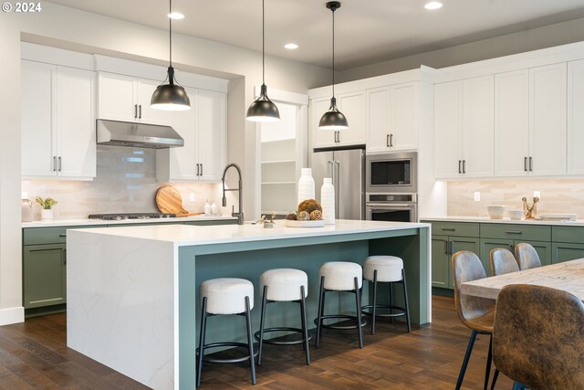 kitchen with stainless steel appliances, a kitchen island with sink, dark wood-type flooring, pendant lighting, and white cabinets