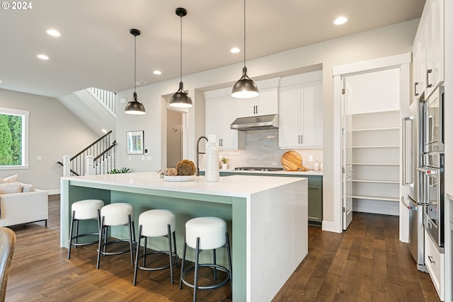 kitchen with white cabinets, hanging light fixtures, a kitchen island with sink, light countertops, and under cabinet range hood